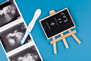 Positive pregnancy test, gynecological ultrasound image, and chalkboard with "1+1=3" written on it. pregnancy, family planning, parenthood, prenatal care and the joy of expecting a baby concept.