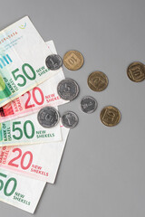 Israel currency 100 and 50 New Israeli shekel (NIS) banknotes alongside agorot coins, on grey background, concept of inflation, economic crisis, rising prices, and financial management.