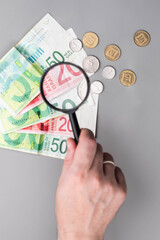 Israel currency 100 and 50 New Israeli shekel (NIS) banknotes and agorot coins under magnifying glass, grey background, concept of inflation, economic crisis, rising prices, and financial management.