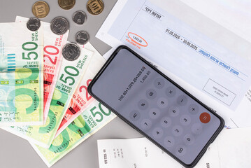 Israel currency New Israeli shekel (NIS) banknotes and agorot coins, with calculator and bills for electricity, water, and taxes, concept of inflation crisis, rising prices, and financial management.