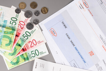 Israel currency New Israeli shekel (NIS) banknotes and agorot coins, with bills for electricity, water, and taxes, concept of inflation, economic crisis, rising prices, and financial management.