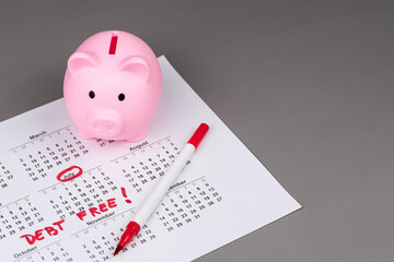 Piggy bank on calendar with the words 'Debt Free' written on it, symbolizing saving money, financial freedom, and achieving a debt-free lifestyle. Concept of financial independence and budgeting.