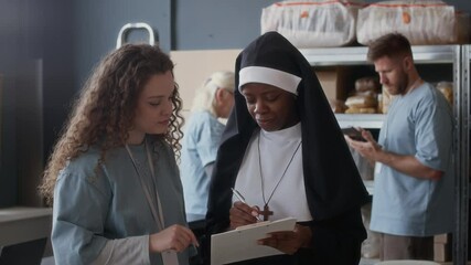 Medium shot of young black nun helping volunteers in donation center with food supplies - Powered by Adobe