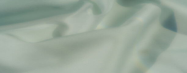 Blur of softly textured pastel green fabric, beautifully capturing subtle drapes and a serene...