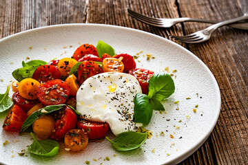 Caprese salad - cherry tomatoes, fresh basil leaves and burrata cheese on wooden background	