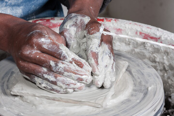 textured strong wet hands immersed in and working with items of pottery moulding clay showing close...