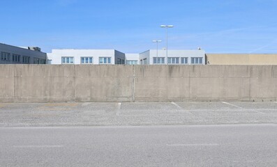 Concrete surrounding wall with industrial building and sky on behind. Street in front. Background...