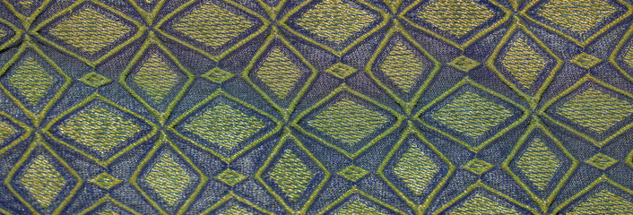 Blur the refined geometry of diamond-shaped embroidery in gold and green on a vivid blue fabric, offering a luxurious touch for decor or fashion-oriented projects.