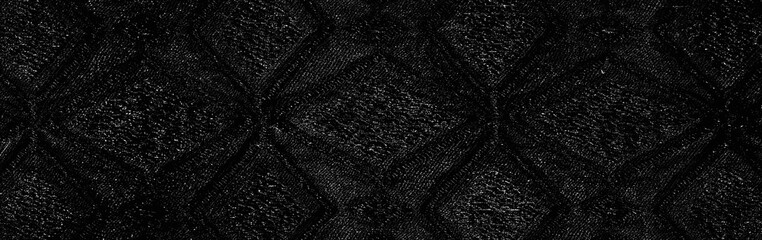 Blurred close-up of folded black fabric with a geometric pattern. The fabric shows a striking contrast between the smoothness of the folds and the textured design