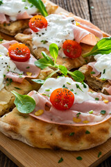 Pinsa Romana with boiled ham, burrata cheese and cherry tomatoes on wooden table	