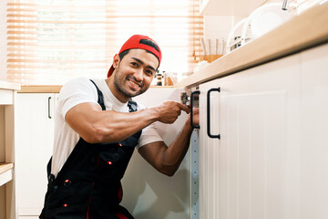 Smiling handyman fixing kitchen cabinet hinges, representing reliable home repair services, maintenance professionalism, and skilled craftsmanship in residential plumbing and handyman business.