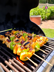 Chicken and bell pepper skewers are grilling over a hot grill outdoors on a sunny day
