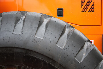 Detailed view of a rugged tire from heavy machinery, showcasing its tread design against an orange...