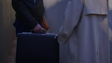 Close up on hands exchanging briefcase and envelope in dark alley street. Night scene with two mysterious business people trading secrets and cash or illegal information. Corruption payment and fraud