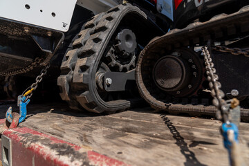 Compact track loader construction machinery tied down with chains and hooks to a construction...