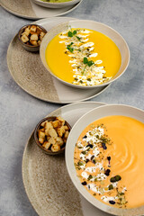 Two creamy pumpkin and sweet potato soups garnished with cream, pumpkin seeds and microgreens, with croutons next to each other on a gray background. Vegan or vegetarian food. Cooking.