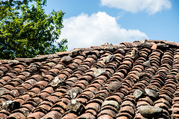 Old tiled countryside house roof with blue sky and white clouds in the background