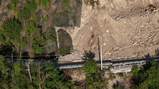 Drone shot of SP21 Vernasca after rockslide on April 22nd 2025, excavators operate to clear blocked road, surrounded by woodland and scattered rocks, real time
