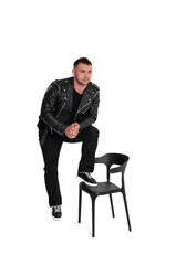 A handsome dark-haired man in a black leather jacket, black T-shirt, trousers and sneakers on a white background