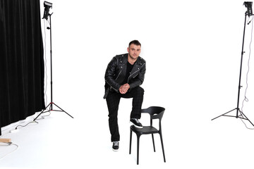 A handsome dark-haired man in a black leather jacket, black T-shirt, trousers and sneakers on a white background