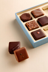 Minimal flatlay of open box with chocolate squares on beige background, elegant candy dessert packaging mockup concept