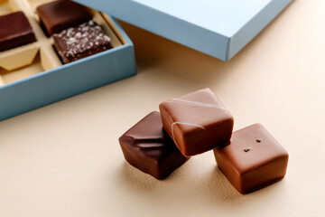 Minimal flatlay of open box with chocolate squares on beige background, elegant candy dessert packaging mockup concept