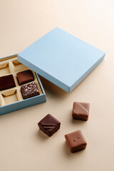 Minimal flatlay of open box with chocolate squares on beige background, elegant candy dessert packaging mockup concept
