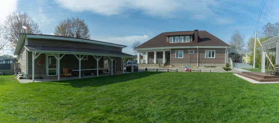 Naklejka premium A beautifully manicured lawn beside a charming home. Perfect picnic spot with a cozy gazebo and shed, surrounded by lush greenery.