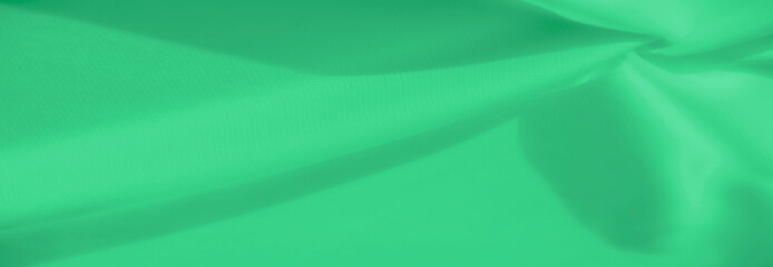 A close-up of a green fabric, showcasing a dynamic interplay of folds and light. The smooth surface...