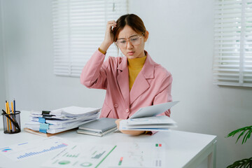 A woman is sitting stressed at a desk with her laptop open and papers scattered around her.