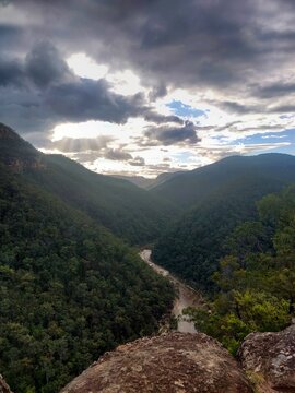 Taken near the Vale of Avoca in Grose Vale, Sydney: View of a river winding through the Blue Mountains on a cloudy day at dusk with the sun shining through.