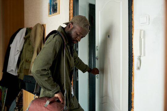 Man in green jacket and cap holding bag, opening door when going to work in morning