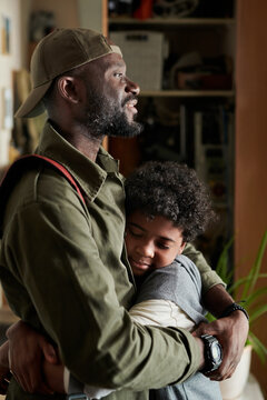 African American father hugging and comforting young son in cozy home environment, both smiling and embracing warmly, forming a strong familial bond with visible affection