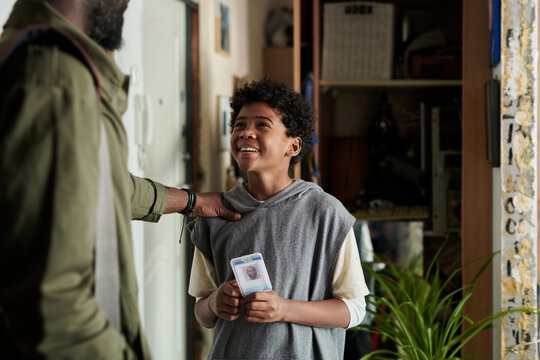Young boy smiling and showing ID card while interacting with dad in indoor setting, with various items in background creating a warm, inviting atmosphere