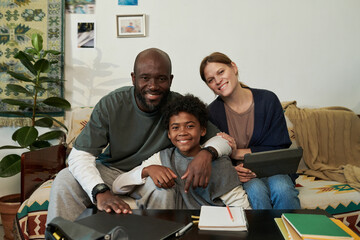 Portrait of happy multiracial family sitting together with smiles, surrounded by homely environment and comfortable seating. Displaying positive emotions and close family bond