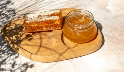 Honey Jar and Honeycomb on Wooden Board. Natural sunlight and long shadows. 