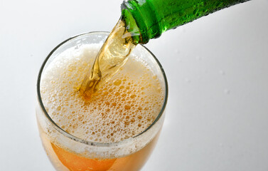 Filling glass with sparkling drink from green bottle
