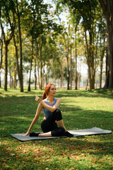 A young woman performs a seated spinal twist yoga pose on a mat in a peaceful, sunlit forest park