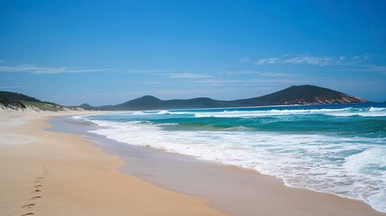 Stunning sandy beach with gentle soft blue ocean waves rolling onto the shore, creating a serene and picturesque coastal scene