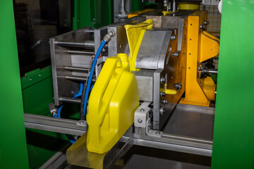 Industrial blow molding machine producing yellow plastic canister. Industrial plastic injection molding process in a factory environment