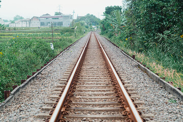 Fototapeta premium A vintage railway track extending into the distance with green foliage on its side