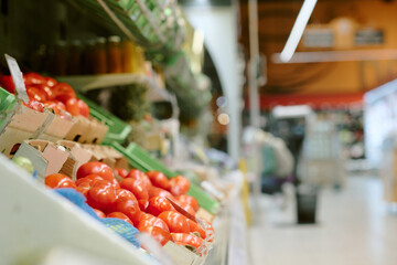Bright red tomatoes displayed in grocery store produce section with various other vegetables and fruits around, offering fresh food choice to shoppers