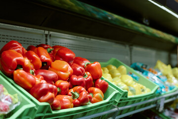 Various colorful bell peppers arranged in green plastic crates at fresh food market. Vegetables like red, yellow, and orange peppers are on display on shelf in grocery store