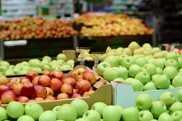 Freshly harvested apples arranged in grocery aisle showcasing variety of types. Green, red, and yellow apples neatly placed in cardboard boxes with blurred background of other produce