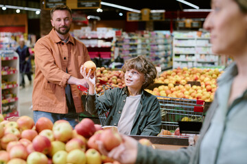 Man and child selecting apples from grocery store produce section. Shelves packed with fruits and vegetables displayed in vibrant environment