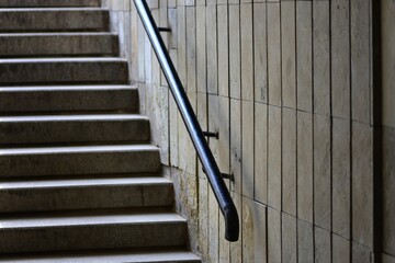 Obraz premium Close-up view of a black metal handrail on a tiled wall beside concrete stairs in an indoor public space. Ideal for themes of architecture, safety, structure, and modern urban design.