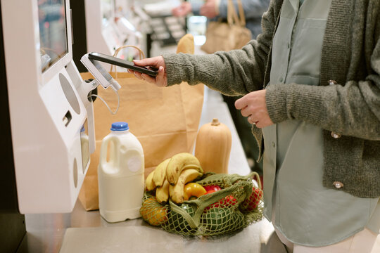 Person using self-checkout machine at grocery store scanning items from shopping basket containing fruits, vegetables and milk
