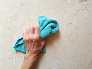 An elderly woman holds a colorful cleaning cloth in her hand. An elderly lady cleans a marble surface