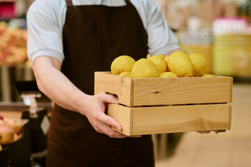 Person carrying crate filled with fresh lemons in vibrant market setting, showcasing healthy and...