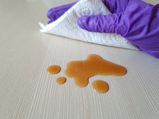 A hand in a protective glove wipes a spilled liquid on a table with a paper napkin